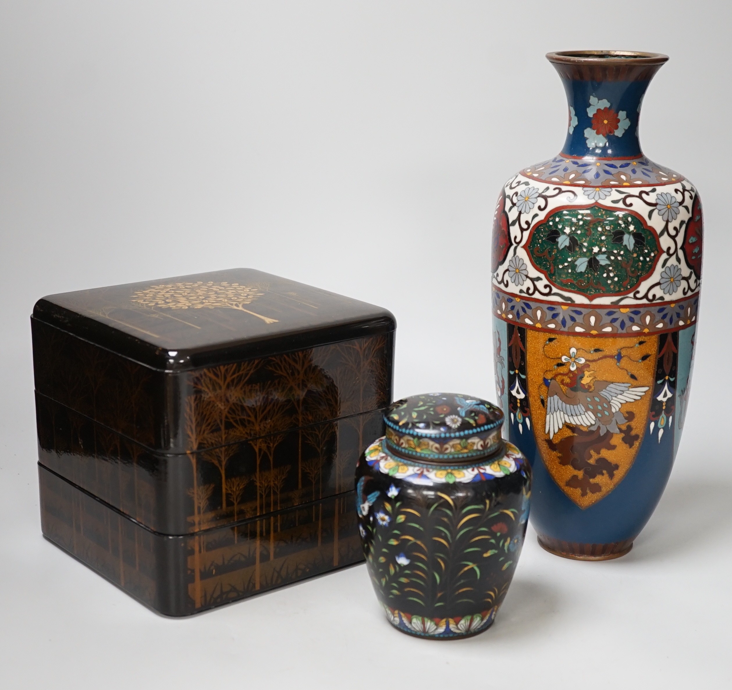 A large Japanese cloisonné enamel vase, 30.5cm high, a similar jar and cover and a Japanese lacquered tiered box with 3-4 drawers. Tree design in gold lacquer.